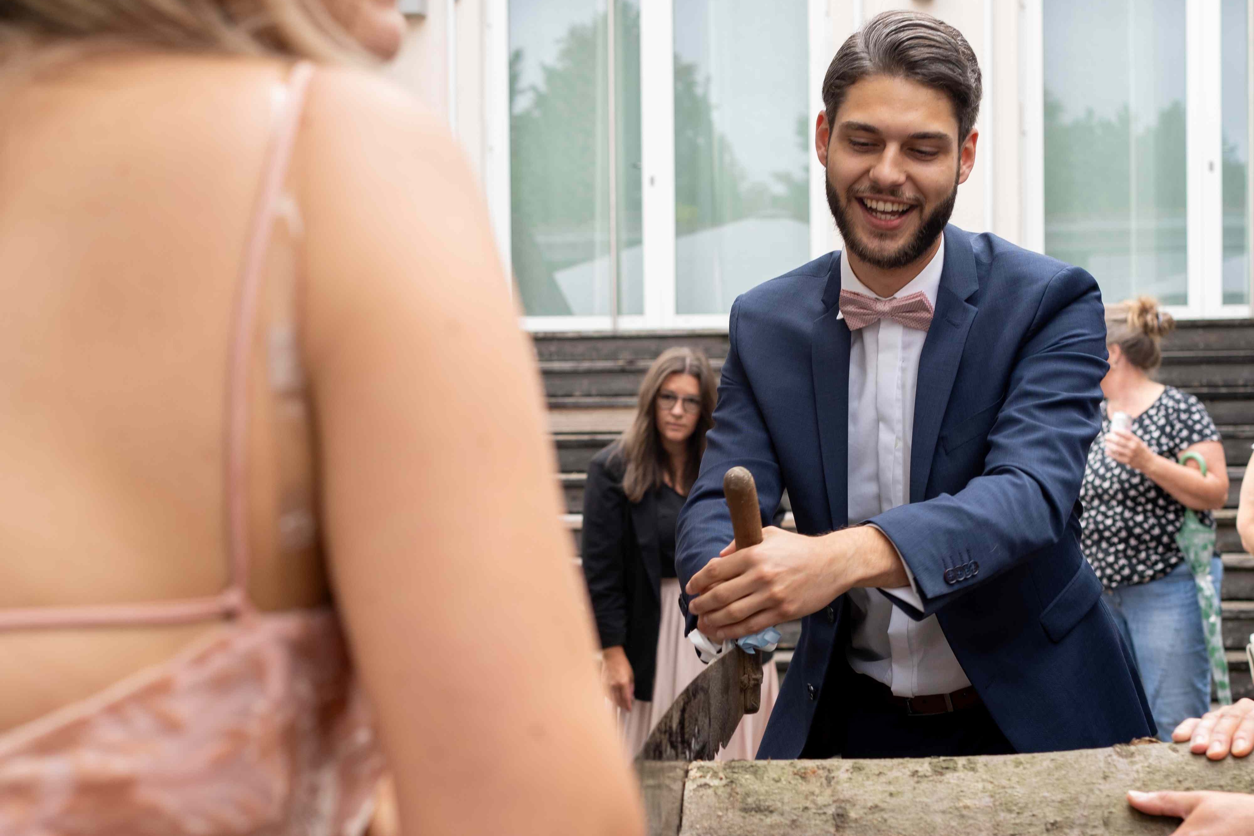 Bräutigam beim traditionellen Baumstammsägen nach der standesamtlichen Trauung in Hessisch Oldendorf – Hochzeitsfoto von René Laeger aus Hameln.