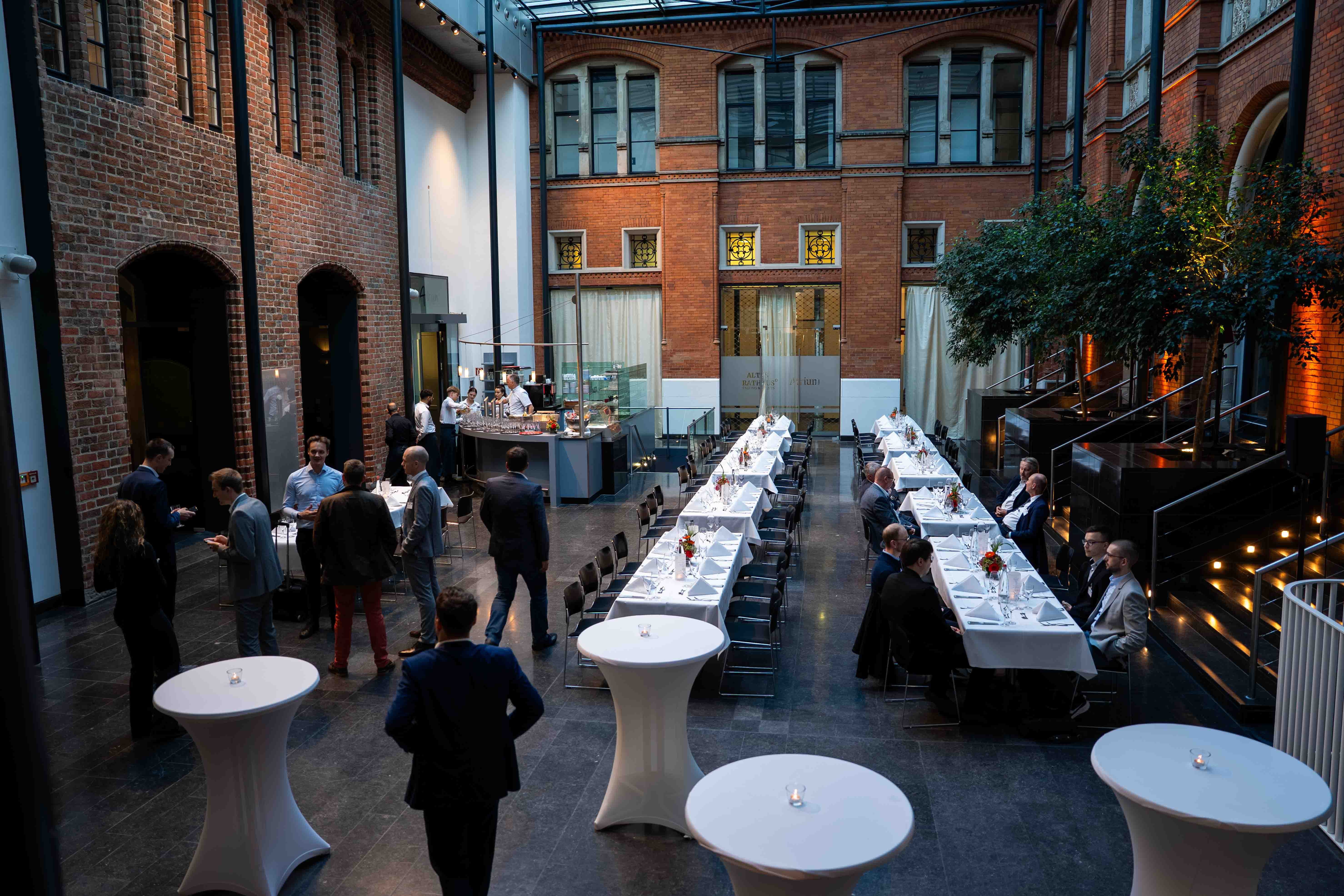 Großer Innenhof mit Glasdach und roten Backsteinwänden, eingerichtet mit langen Dinnertafeln und Stehtischen.