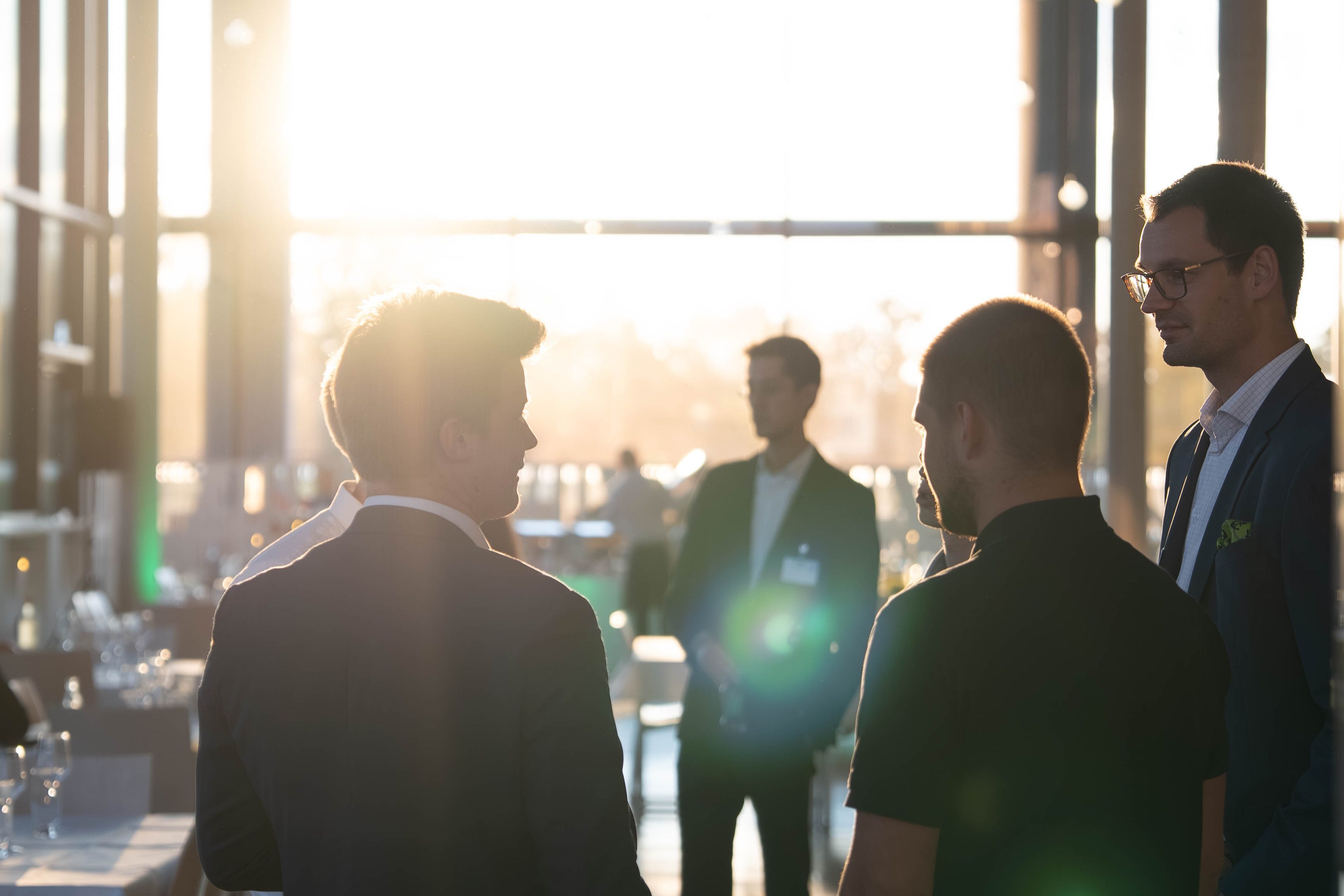 Silhouetten einer Gruppe von Männern im Gespräch, die vor einem großen Fenster im Sonnenuntergang stehen.
